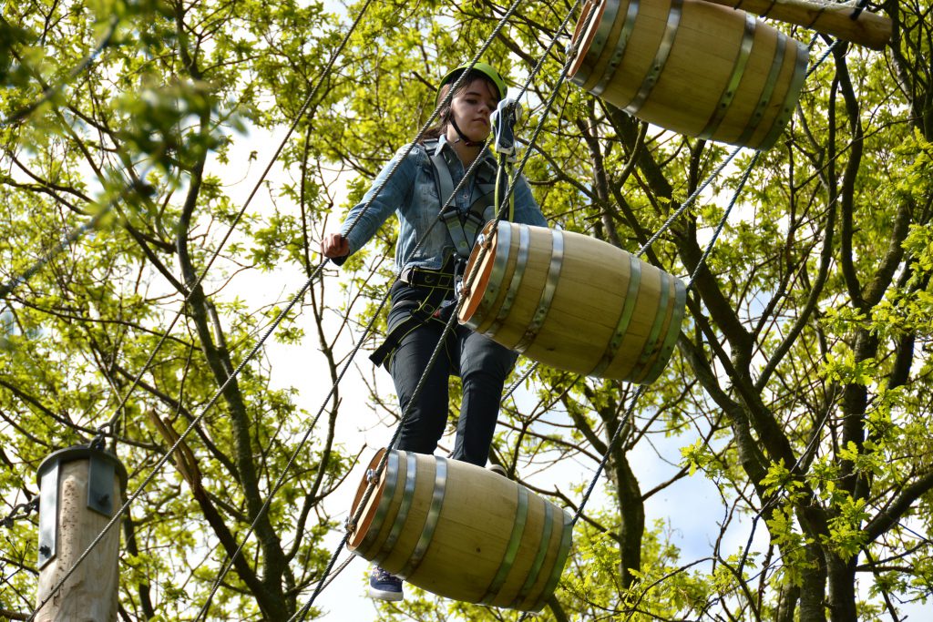 Meisje klimt over de tonnen op 12 meter hoogte bij Klimpark Streekbos